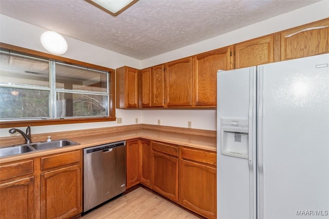 kitchen with white refrigerator with ice dispenser, light countertops, a textured ceiling, stainless steel dishwasher, and a sink