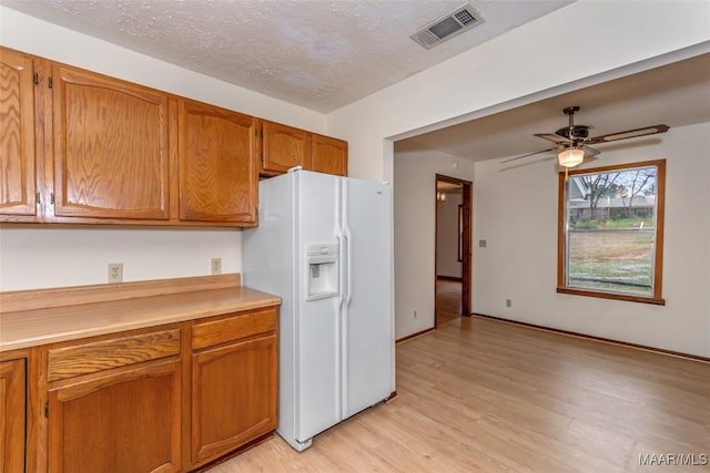 kitchen featuring light countertops, visible vents, brown cabinetry, light wood-style floors, and white fridge with ice dispenser