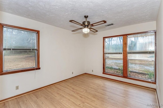 empty room with a wealth of natural light, light wood-style flooring, visible vents, and baseboards