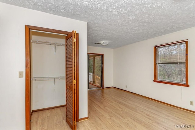 unfurnished bedroom with light wood-type flooring, a textured ceiling, baseboards, and a closet