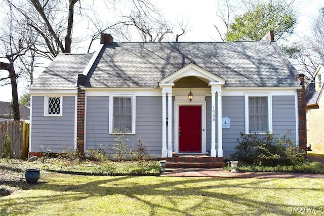 view of front facade with roof with shingles, a front lawn, a chimney, and fence