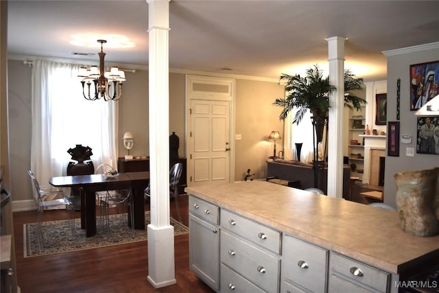 kitchen with ornamental molding, dark wood-type flooring, light countertops, ornate columns, and a chandelier