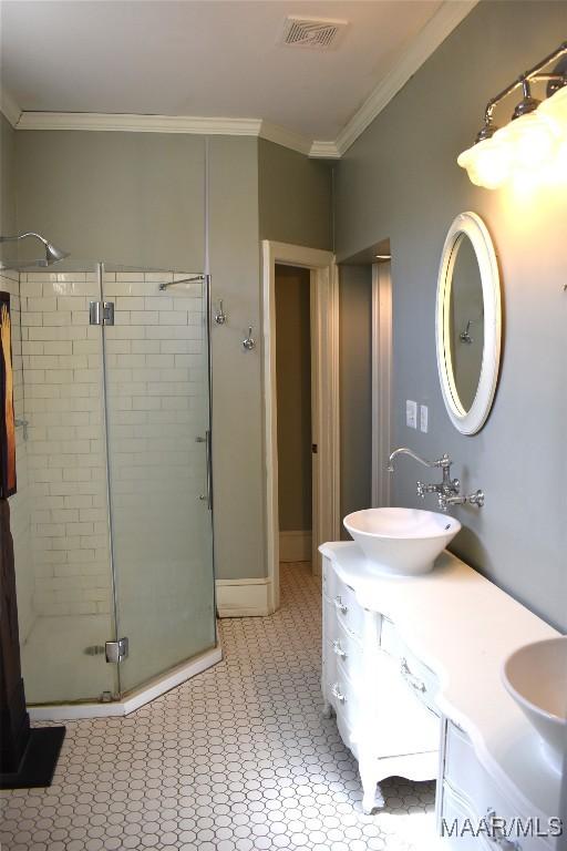 bathroom with a stall shower, crown molding, visible vents, and a sink