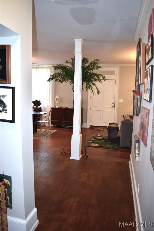 corridor featuring baseboards, crown molding, wood finished floors, and ornate columns