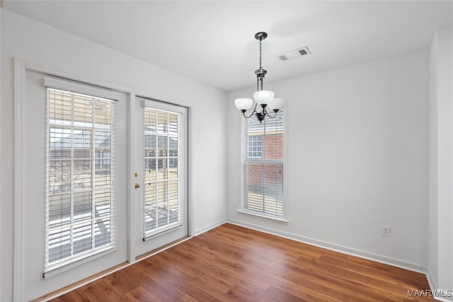 unfurnished dining area with baseboards, visible vents, an inviting chandelier, and wood finished floors