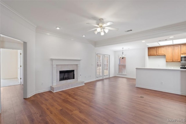 unfurnished living room with visible vents, a tiled fireplace, ornamental molding, wood finished floors, and ceiling fan with notable chandelier