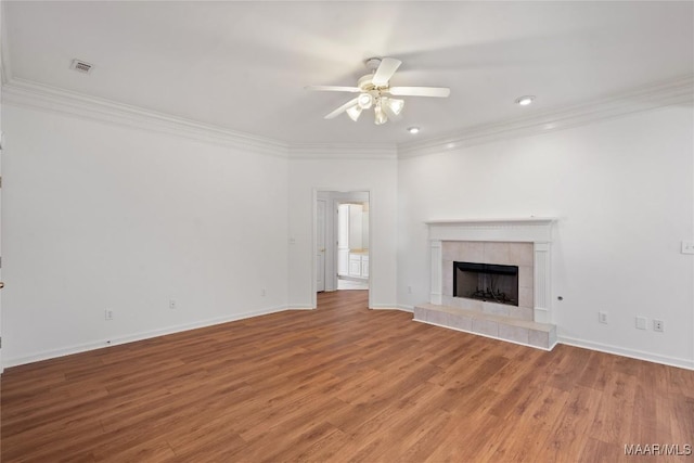 unfurnished living room with visible vents, a tiled fireplace, ornamental molding, a ceiling fan, and wood finished floors