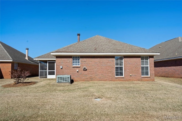 rear view of house with brick siding, a shingled roof, a lawn, a sunroom, and central AC