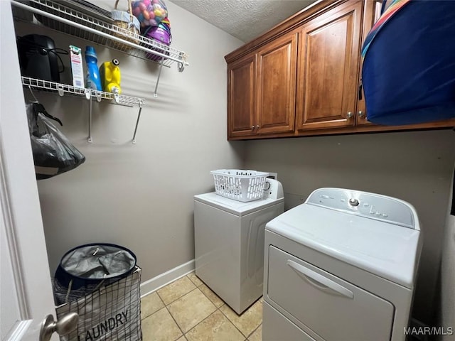 laundry area featuring light tile patterned floors, cabinet space, washing machine and dryer, a textured ceiling, and baseboards