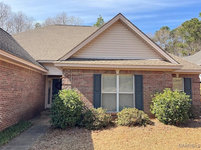 view of side of home featuring roof with shingles and brick siding