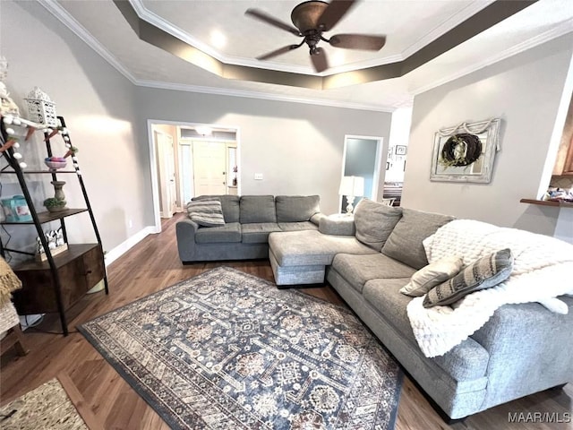 living room with wood finished floors, a ceiling fan, baseboards, ornamental molding, and a raised ceiling