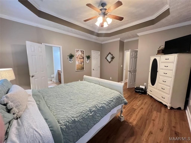 bedroom featuring a tray ceiling, crown molding, ceiling fan, ensuite bath, and wood finished floors