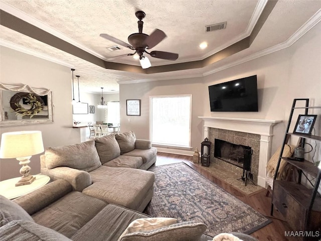 living area featuring a raised ceiling, visible vents, a tiled fireplace, and wood finished floors