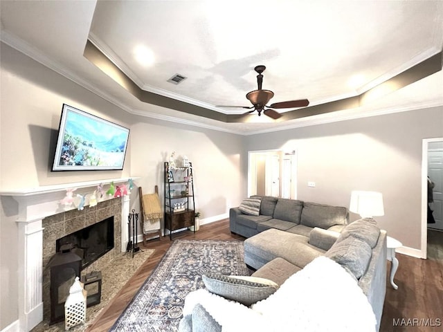 living room with crown molding, a fireplace, a raised ceiling, wood finished floors, and baseboards