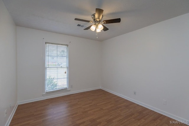 empty room featuring a ceiling fan, visible vents, baseboards, and wood finished floors