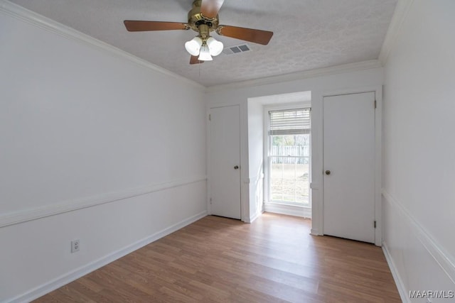 unfurnished room with crown molding, visible vents, a textured ceiling, wood finished floors, and baseboards