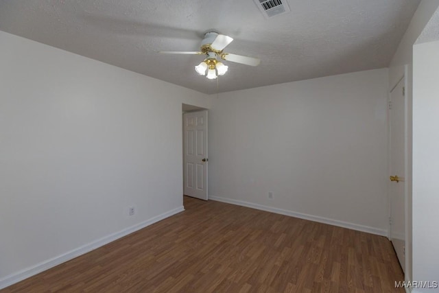 spare room with a textured ceiling, wood finished floors, visible vents, and baseboards