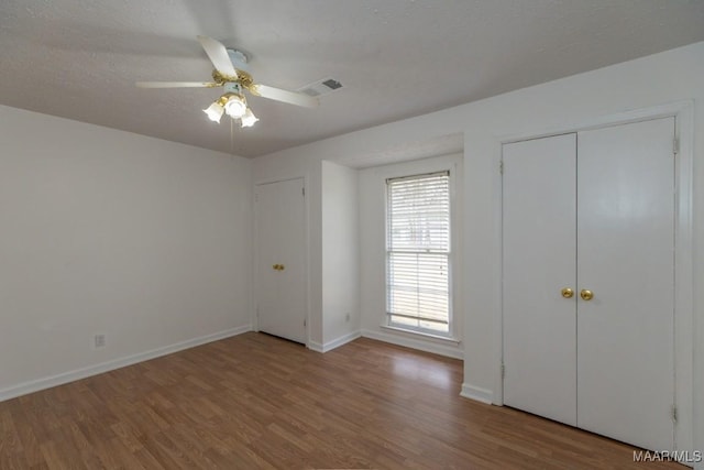 unfurnished bedroom featuring visible vents, ceiling fan, a textured ceiling, wood finished floors, and baseboards