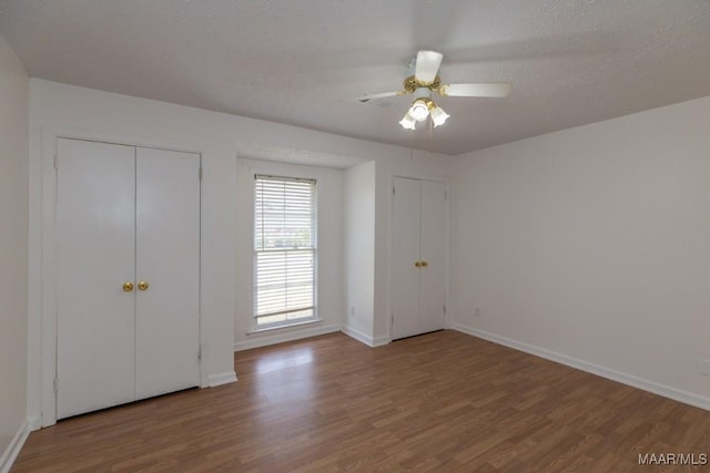 unfurnished bedroom featuring a textured ceiling, wood finished floors, a ceiling fan, baseboards, and two closets