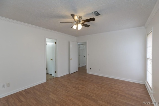 spare room featuring crown molding, visible vents, a textured ceiling, wood finished floors, and baseboards