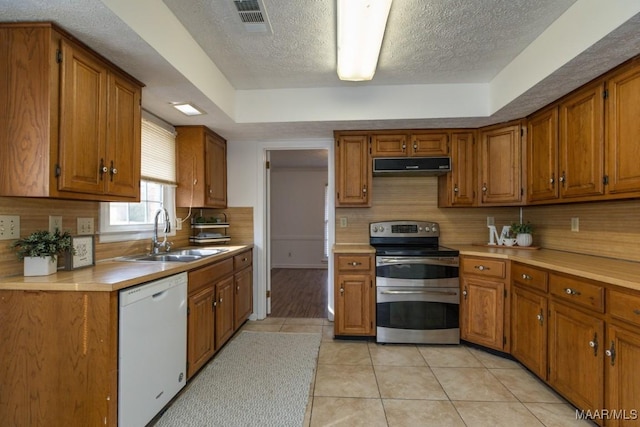 kitchen featuring dishwasher, brown cabinets, under cabinet range hood, double oven range, and a sink