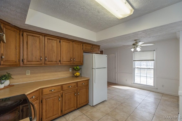 kitchen with a ceiling fan, brown cabinets, light countertops, and freestanding refrigerator