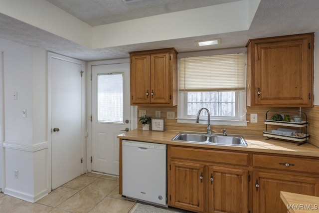 kitchen featuring brown cabinets, light countertops, white dishwasher, and a sink