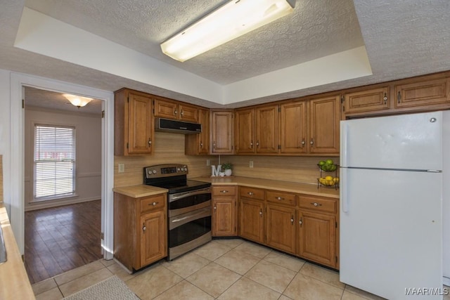 kitchen featuring under cabinet range hood, brown cabinetry, freestanding refrigerator, and double oven range