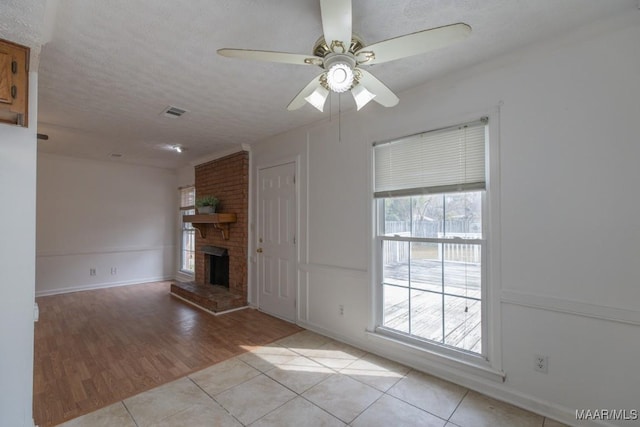 unfurnished living room with a brick fireplace, light tile patterned floors, visible vents, and a textured ceiling