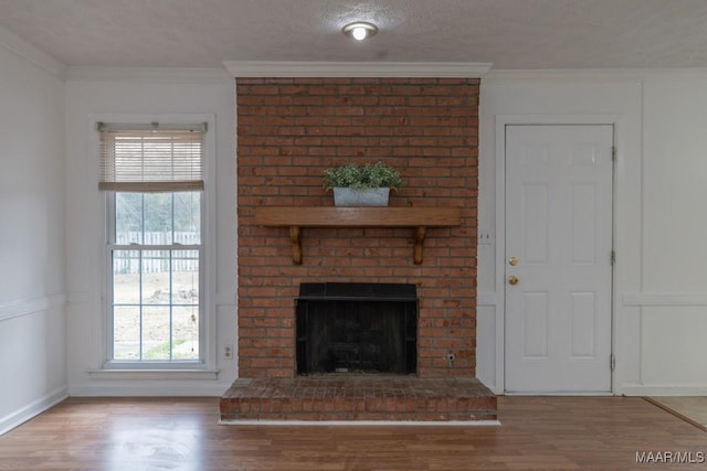 unfurnished living room featuring a textured ceiling, a fireplace, wood finished floors, and crown molding