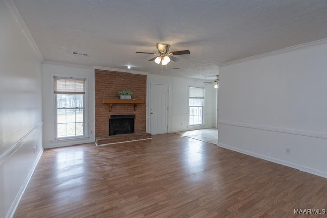 unfurnished living room with ornamental molding, visible vents, a fireplace, and wood finished floors