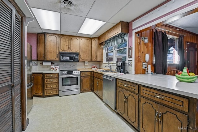 kitchen featuring stainless steel appliances, a sink, light countertops, light floors, and brown cabinetry