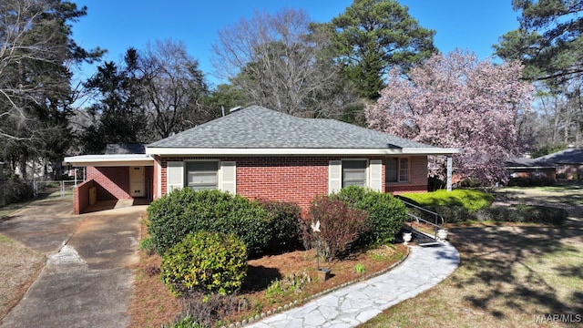 ranch-style house with a carport, concrete driveway, brick siding, and a shingled roof