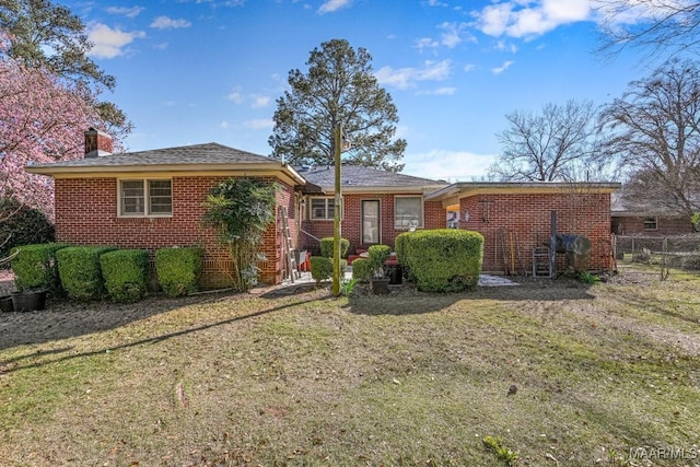 view of front of home with brick siding, a chimney, fence, and a front yard