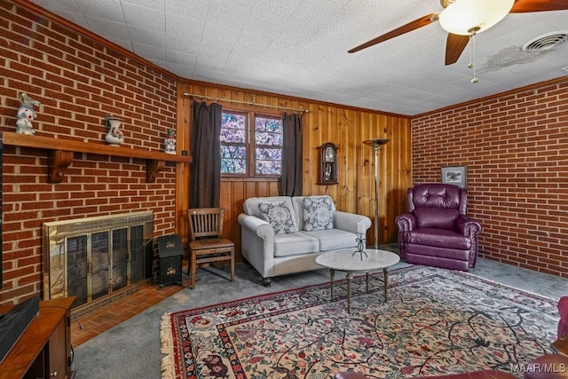 carpeted living room featuring visible vents, a ceiling fan, brick wall, ornamental molding, and a brick fireplace