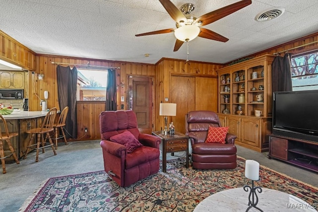 carpeted living area with a healthy amount of sunlight, wood walls, visible vents, and ornamental molding
