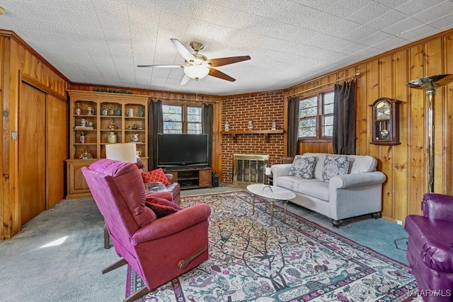 carpeted living area with a brick fireplace, a healthy amount of sunlight, wood walls, and ceiling fan
