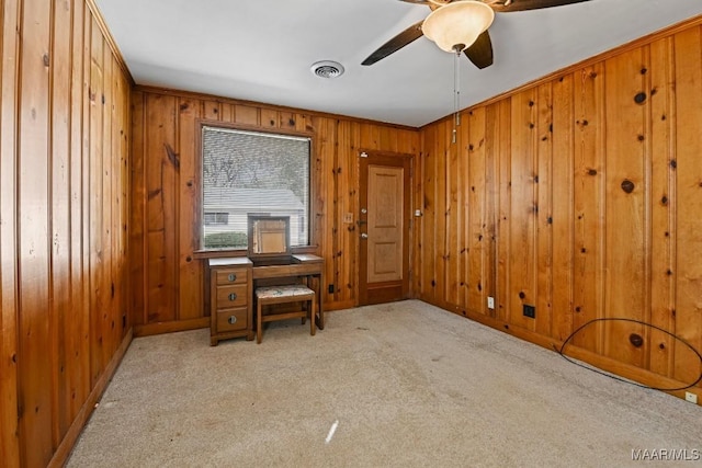 carpeted spare room featuring baseboards, a ceiling fan, visible vents, and wooden walls