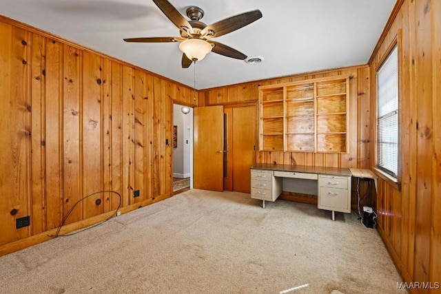 unfurnished office with wooden walls, visible vents, a ceiling fan, crown molding, and carpet floors
