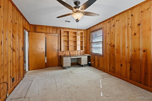unfurnished office featuring carpet floors, ornamental molding, wooden walls, and ceiling fan
