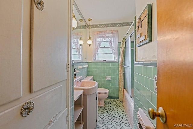 full bath with toilet, a wainscoted wall, shower / bath combination with glass door, vanity, and tile walls