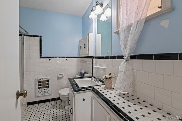 bathroom featuring toilet, a wainscoted wall, tile walls, vanity, and heating unit