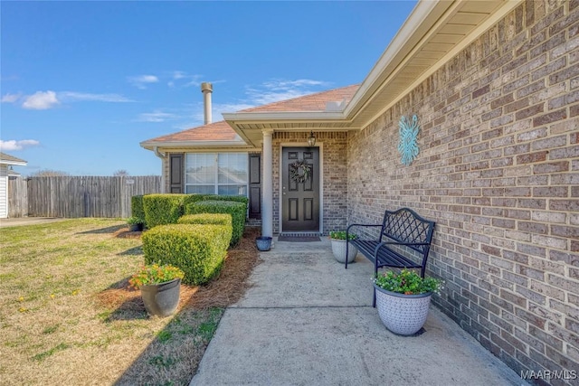 view of exterior entry featuring brick siding and fence