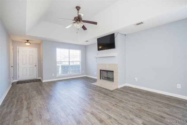 unfurnished living room with baseboards, visible vents, a tile fireplace, wood finished floors, and a tray ceiling