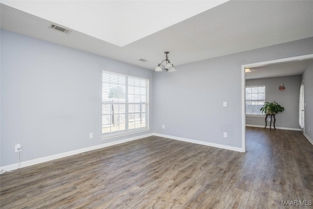 empty room featuring a notable chandelier, dark wood finished floors, visible vents, and baseboards