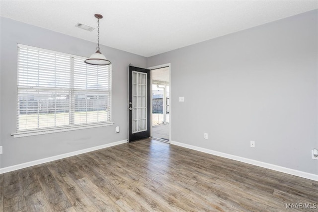 empty room with wood finished floors, visible vents, and baseboards