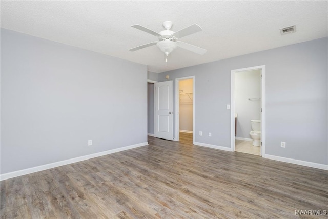 unfurnished bedroom featuring visible vents, a spacious closet, baseboards, and wood finished floors