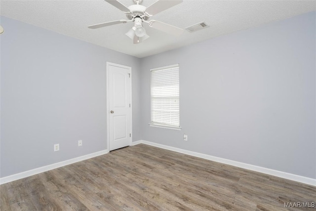 empty room with a ceiling fan, baseboards, visible vents, and wood finished floors