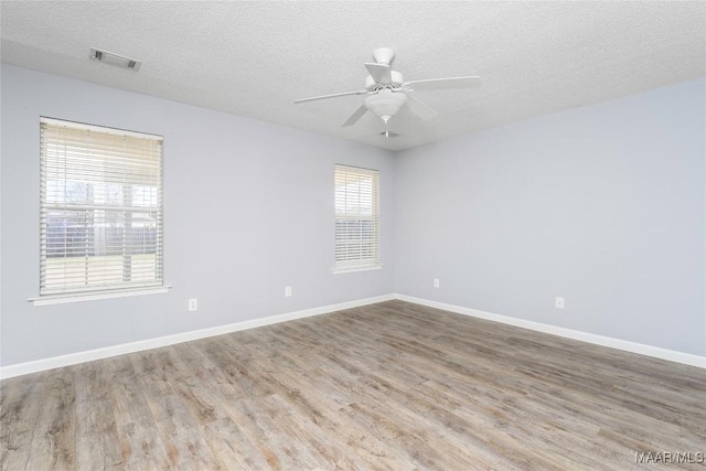 spare room featuring a ceiling fan, baseboards, visible vents, and wood finished floors