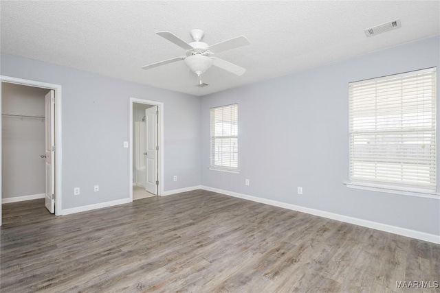 unfurnished bedroom with a textured ceiling, wood finished floors, visible vents, and a walk in closet